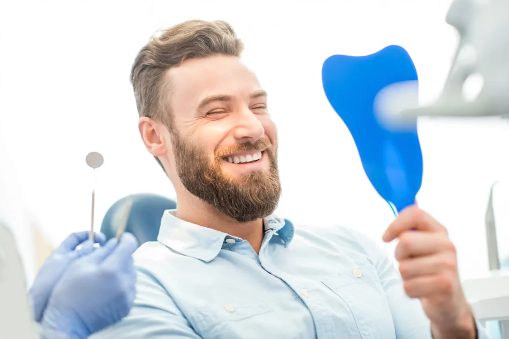 man looking at mirror to observe his clean teeth at dental office